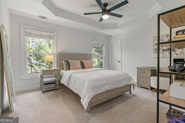 bedroom with a tray ceiling, light colored carpet, ornamental molding, baseboards, and visible vents