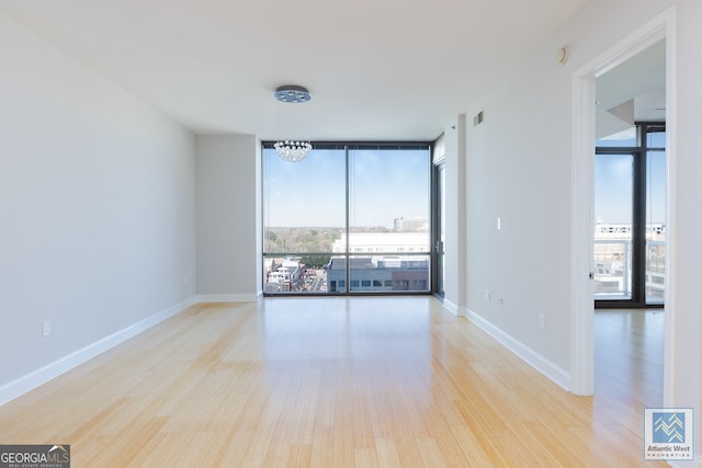 unfurnished room with visible vents, expansive windows, baseboards, and wood finished floors