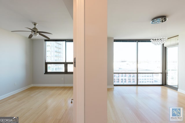 unfurnished room featuring ceiling fan with notable chandelier, expansive windows, baseboards, and wood finished floors