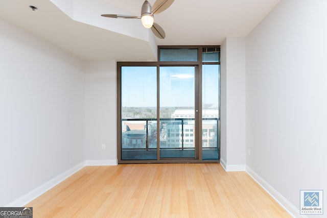 spare room with baseboards, wood finished floors, a ceiling fan, and floor to ceiling windows