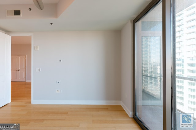 empty room featuring a wall of windows, visible vents, light wood-style flooring, and baseboards