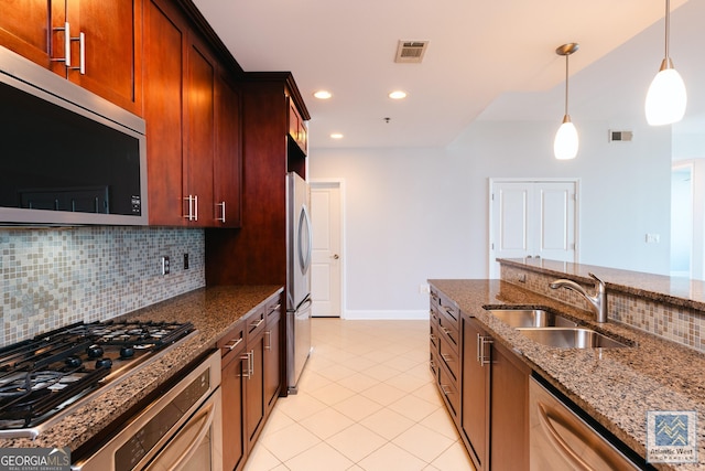 kitchen featuring visible vents, appliances with stainless steel finishes, dark stone countertops, hanging light fixtures, and a sink