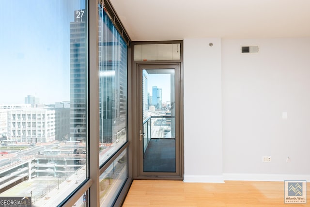 doorway with a view of city, visible vents, light wood-style flooring, and baseboards