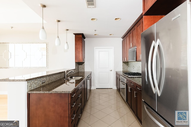 kitchen with stainless steel appliances, a peninsula, a sink, tasteful backsplash, and dark stone countertops