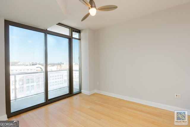 spare room featuring baseboards, ceiling fan, a view of city, a wall of windows, and light wood-style floors