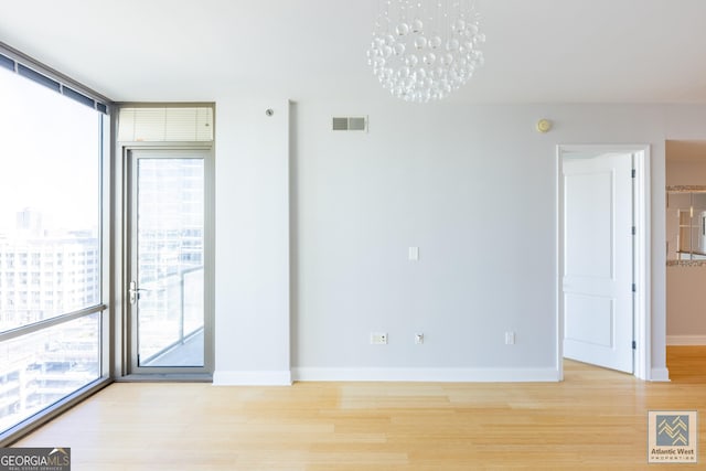 spare room with light wood-style flooring, a wall of windows, visible vents, and baseboards