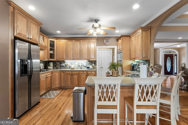 kitchen with decorative backsplash, a peninsula, stainless steel appliances, light wood-style floors, and a sink