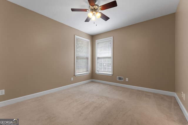 empty room with baseboards, visible vents, ceiling fan, and light colored carpet