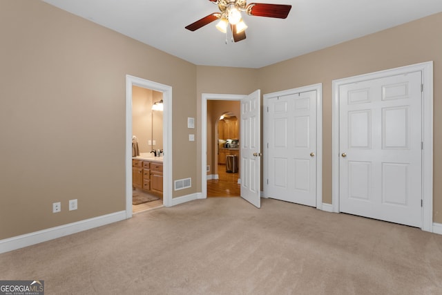 unfurnished bedroom featuring baseboards, ensuite bath, visible vents, and light colored carpet