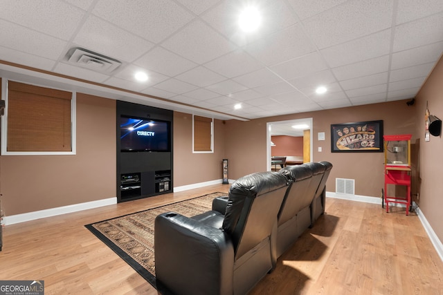 cinema room with a paneled ceiling, visible vents, light wood-style flooring, and baseboards