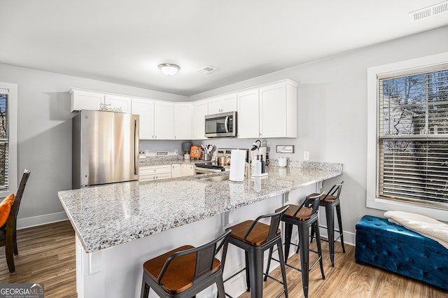 kitchen featuring a peninsula, visible vents, stainless steel appliances, and white cabinets