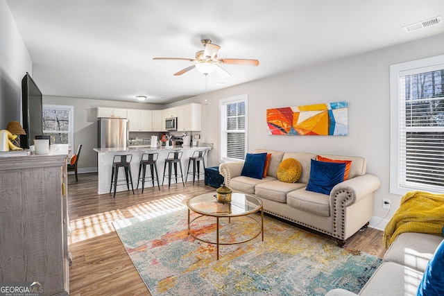 living area featuring baseboards, visible vents, a ceiling fan, and wood finished floors