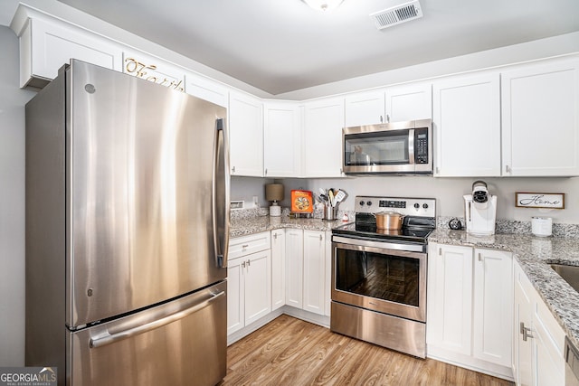 kitchen with light wood finished floors, visible vents, white cabinets, appliances with stainless steel finishes, and light stone countertops