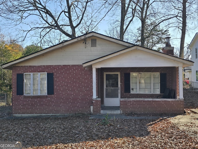 view of front facade with covered porch, a chimney, and brick siding