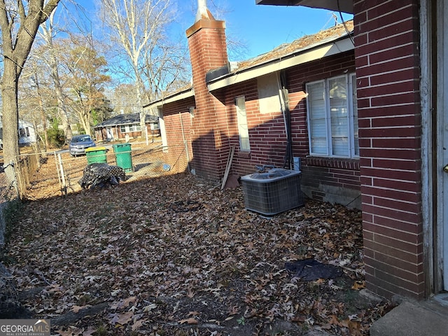 view of home's exterior with brick siding, a chimney, cooling unit, and fence