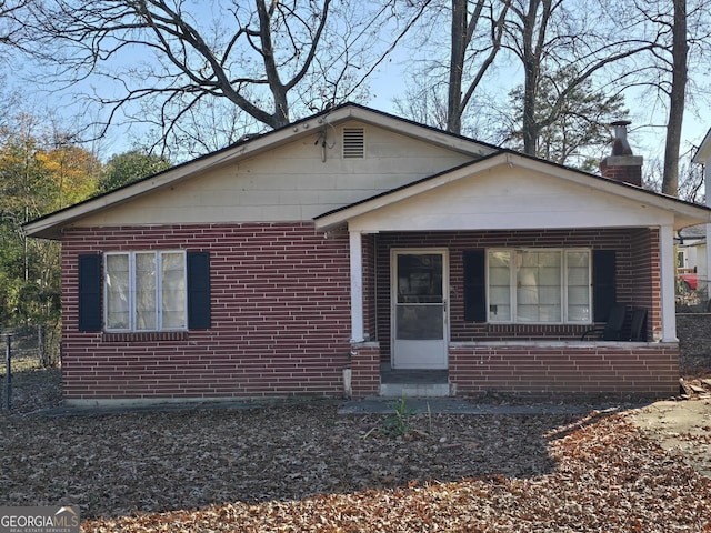 bungalow-style home featuring a chimney, a porch, and brick siding