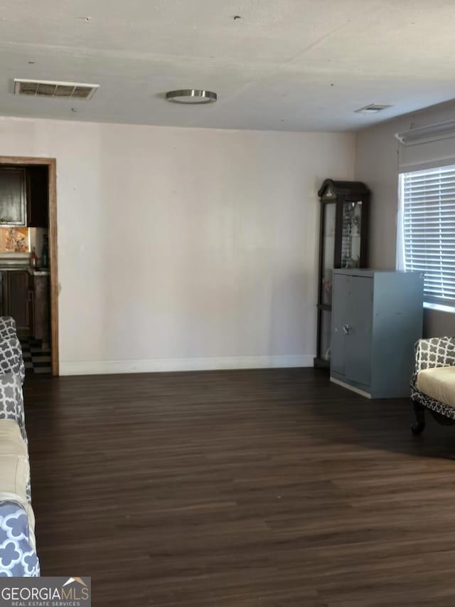 unfurnished living room with dark wood-style floors, visible vents, and baseboards