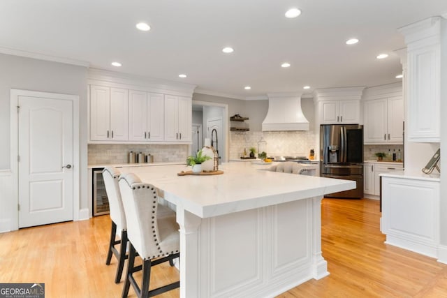 kitchen with premium range hood, wine cooler, white cabinets, and black fridge with ice dispenser