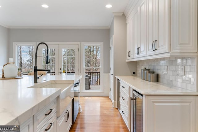 kitchen with beverage cooler, light wood finished floors, light stone countertops, and crown molding