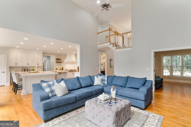 living area featuring recessed lighting, stairway, light wood-style flooring, a high ceiling, and ceiling fan with notable chandelier