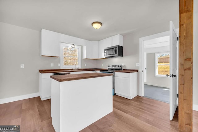 kitchen featuring a kitchen island, wood counters, white cabinetry, appliances with stainless steel finishes, and light wood finished floors