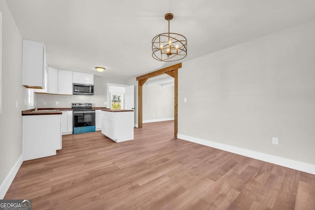 kitchen featuring stainless steel appliances, white cabinets, open floor plan, light wood-type flooring, and dark countertops