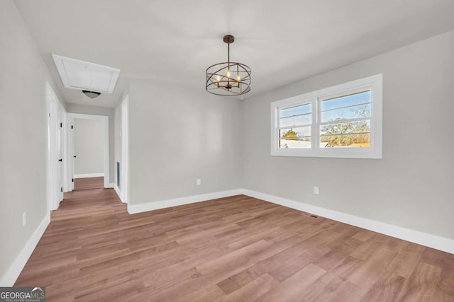 unfurnished dining area with a chandelier, light wood-style flooring, attic access, and baseboards