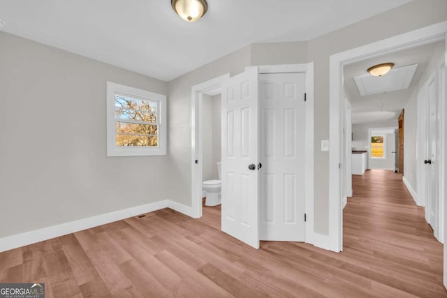 unfurnished bedroom featuring light wood-type flooring, attic access, baseboards, and a closet