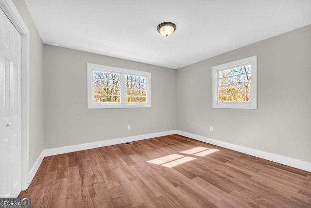 unfurnished bedroom featuring wood finished floors, multiple windows, a closet, and baseboards