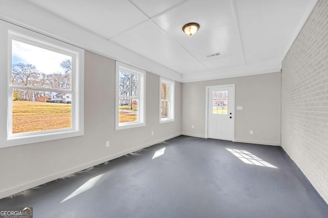 empty room featuring concrete flooring, brick wall, visible vents, and baseboards