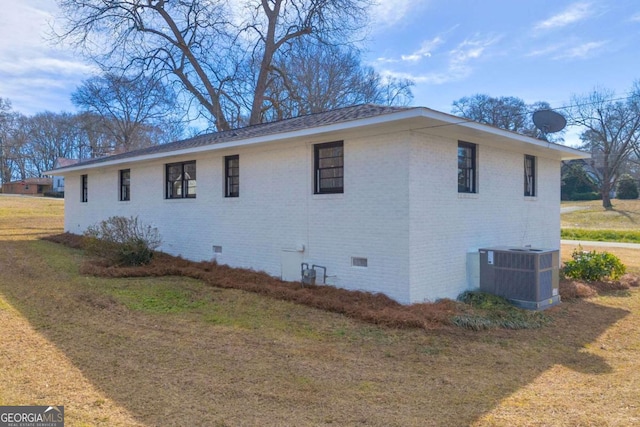 view of side of home with brick siding, crawl space, a lawn, and central air condition unit