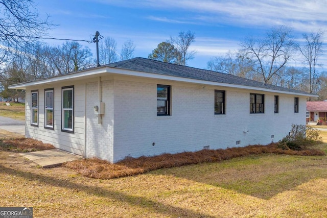 view of side of home with a shingled roof, crawl space, brick siding, and a lawn