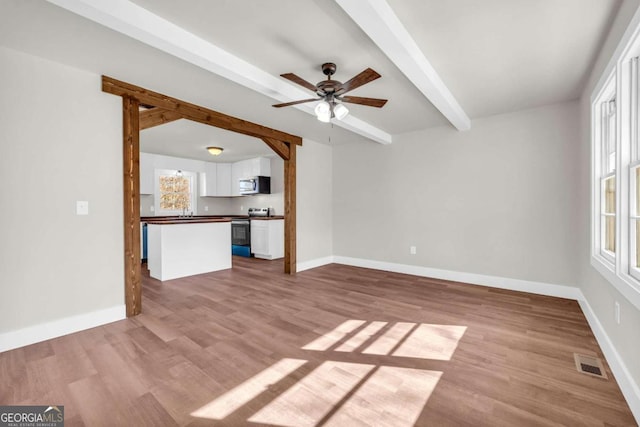 unfurnished living room featuring plenty of natural light, beamed ceiling, and wood finished floors