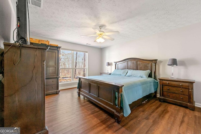 bedroom with visible vents, dark wood finished floors, a textured ceiling, and baseboards