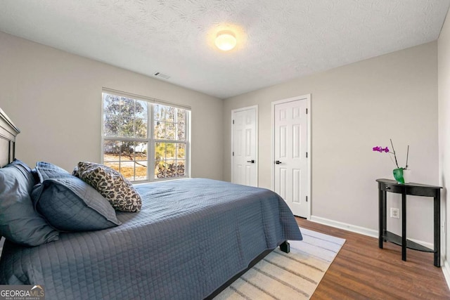 bedroom with a textured ceiling, wood finished floors, visible vents, and baseboards