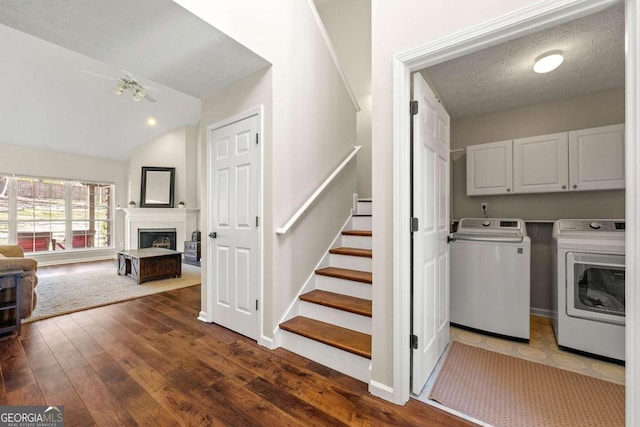 laundry room with dark wood-style floors, a fireplace, cabinet space, washing machine and dryer, and a textured ceiling