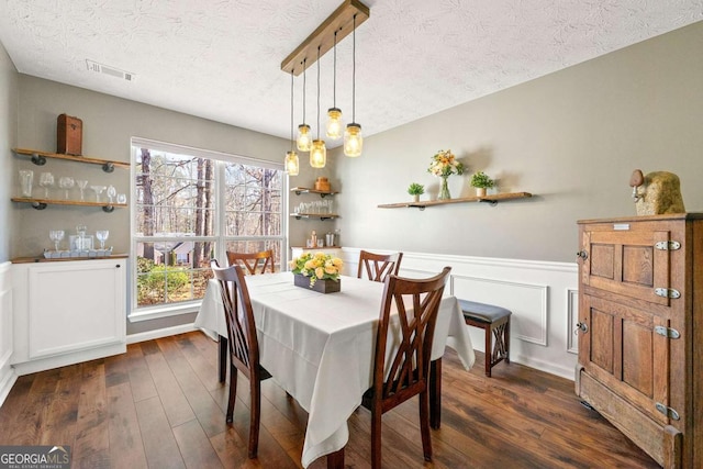 dining area with a textured ceiling, visible vents, dark wood-type flooring, and wainscoting