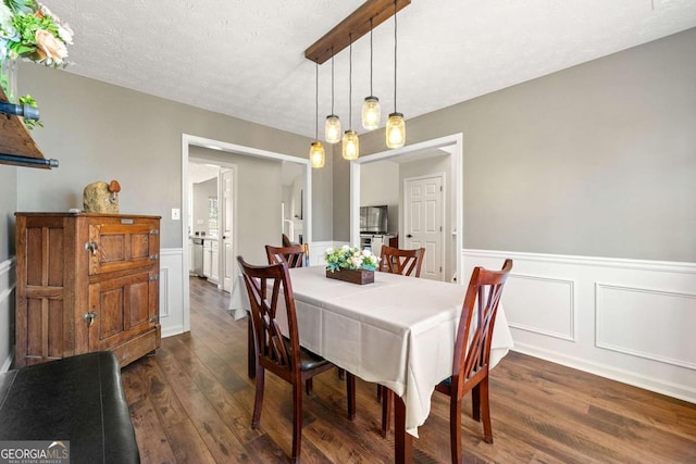 dining space featuring a wainscoted wall, dark wood finished floors, and a textured ceiling