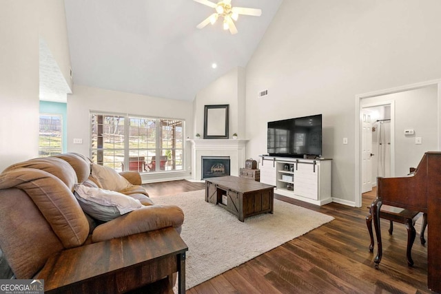 living area with visible vents, baseboards, a fireplace with flush hearth, dark wood-type flooring, and high vaulted ceiling