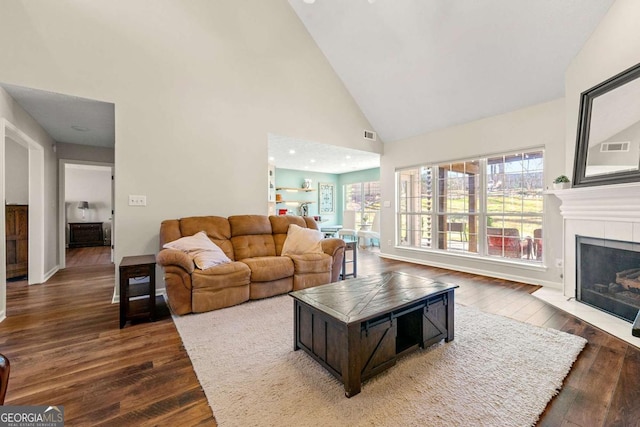 living room featuring dark wood-type flooring, baseboards, high vaulted ceiling, and a tiled fireplace