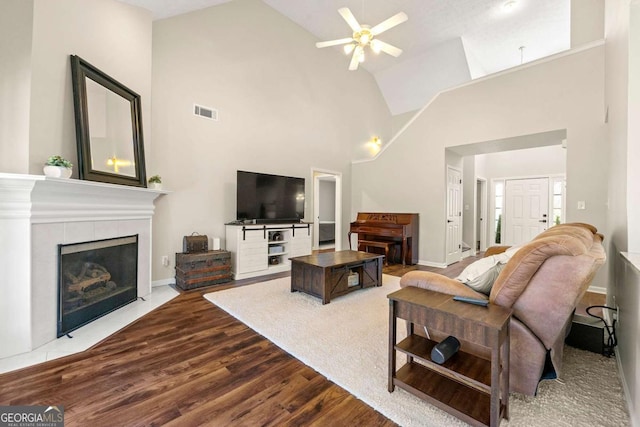 living room with visible vents, a tiled fireplace, dark wood-type flooring, a ceiling fan, and baseboards