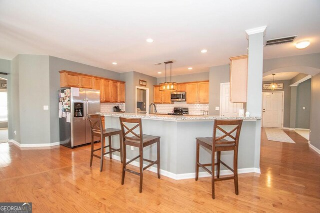 kitchen featuring arched walkways, light wood finished floors, a breakfast bar area, stainless steel appliances, and visible vents