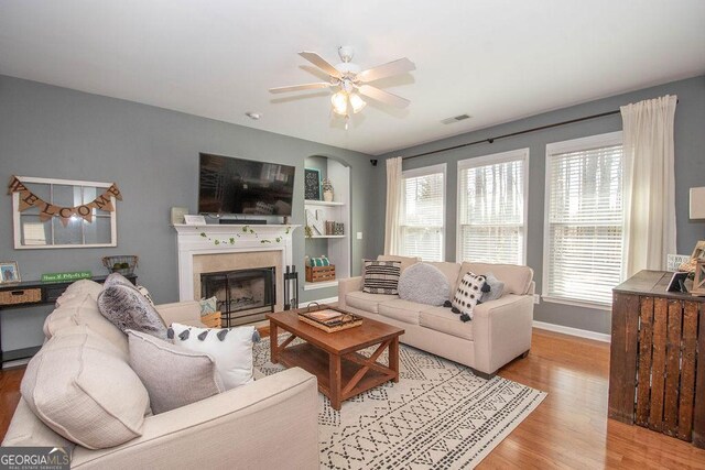 living room featuring a fireplace, visible vents, ceiling fan, wood finished floors, and baseboards