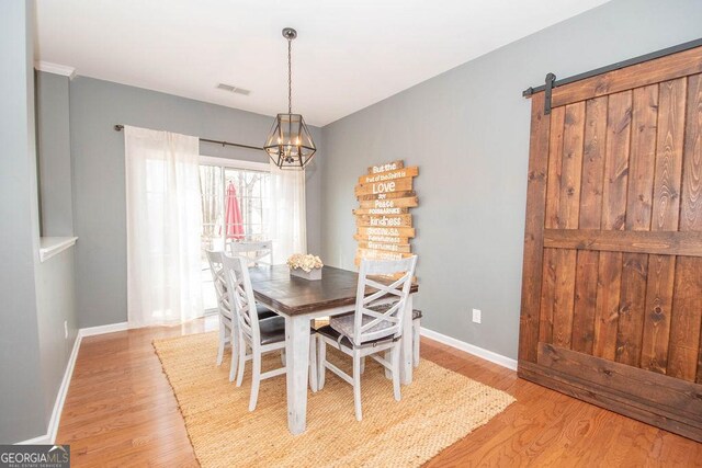 dining space with visible vents, a barn door, a chandelier, light wood-type flooring, and baseboards