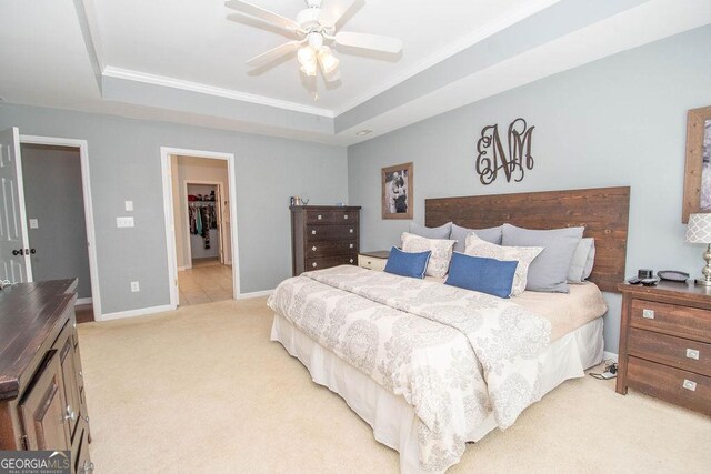 bedroom featuring baseboards, a ceiling fan, light colored carpet, a spacious closet, and a tray ceiling