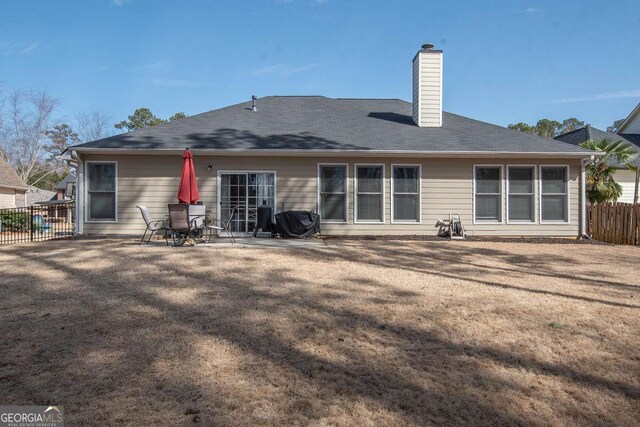 rear view of house featuring a chimney, fence, a lawn, and a patio