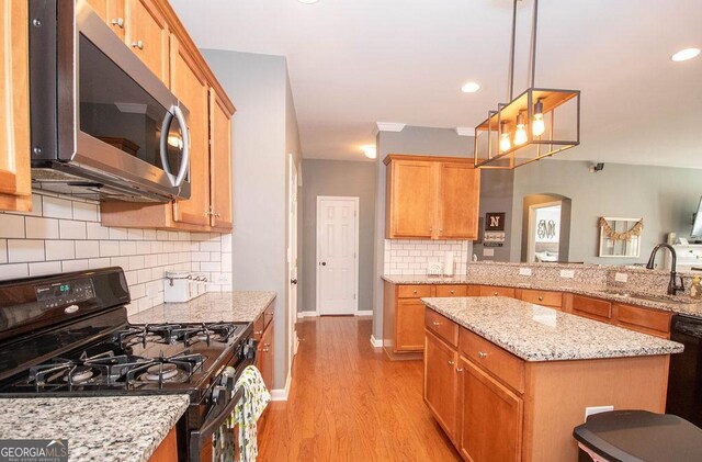 kitchen with a sink, baseboards, light wood-type flooring, light stone countertops, and black appliances