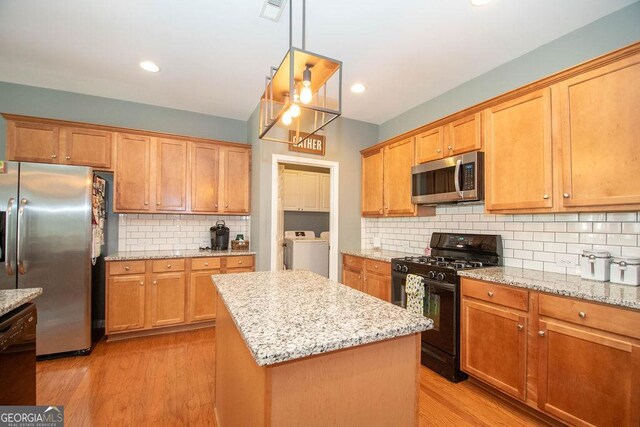 kitchen with light wood finished floors, visible vents, light stone counters, black appliances, and washing machine and dryer