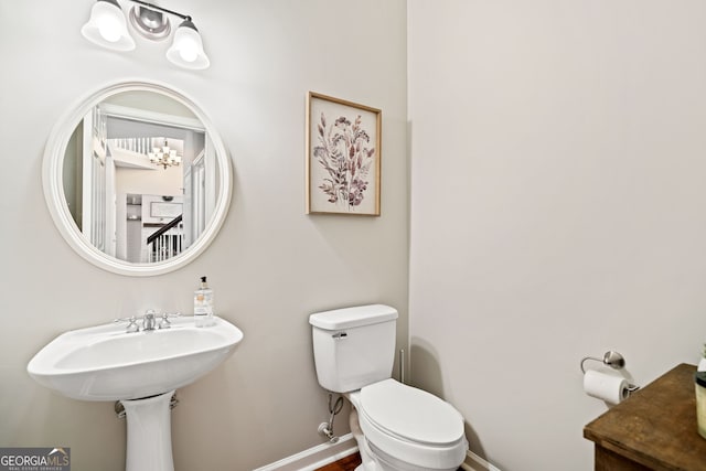 half bathroom featuring a notable chandelier, baseboards, and toilet