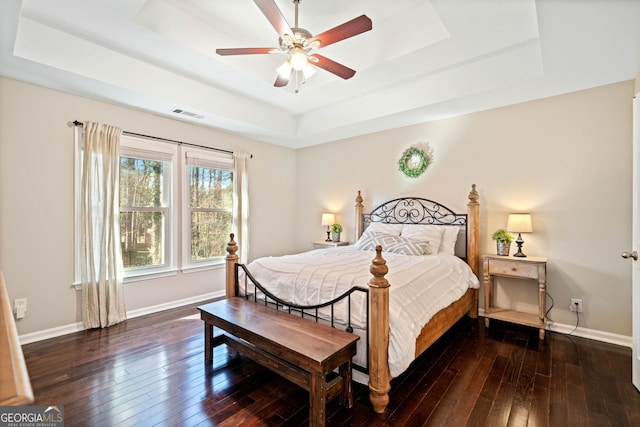 bedroom featuring visible vents, ceiling fan, baseboards, a tray ceiling, and hardwood / wood-style floors